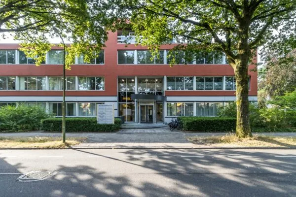 Voorgevel van een modern kantoorgebouw aan de Jan van Eycklaan met een glazen entree, omlijst door bomen en groen.